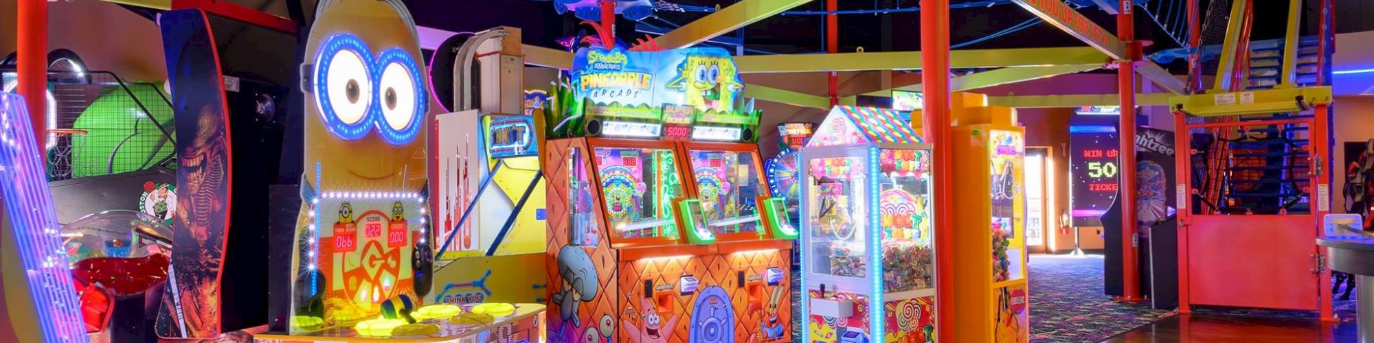 This image shows a vibrant arcade filled with various games, colorful lights, and a high rope course structure overhead.