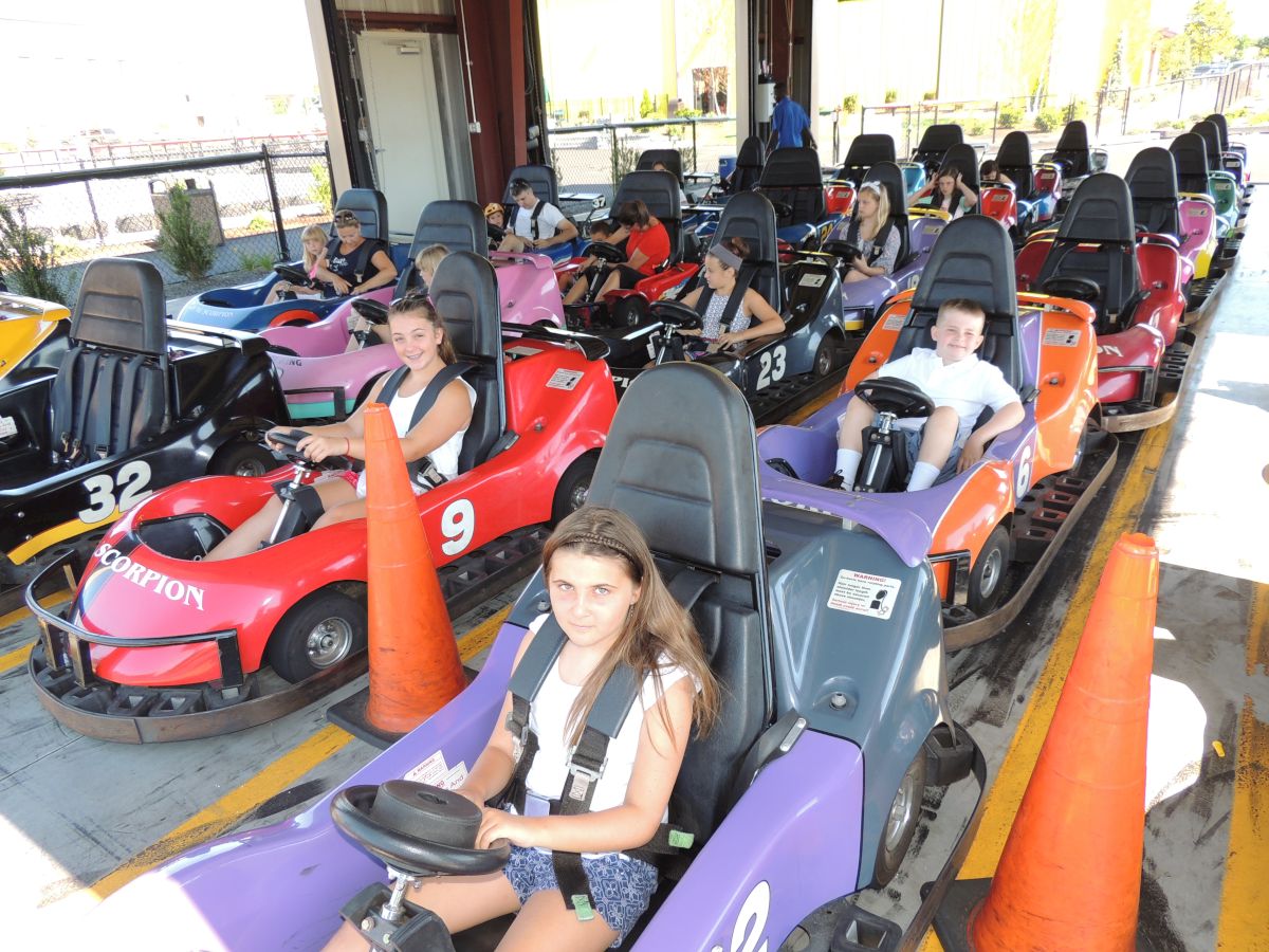 A group of kids and adults are seated in go-karts, ready to race on a go-kart track, surrounded by traffic cones.