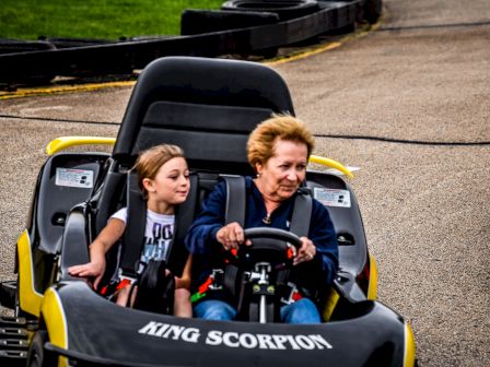 Two people, an adult and a child, are riding in a go-kart labeled 