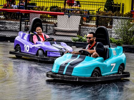 Two people are racing in colorful bumper cars; one in a purple car, the other in a blue car numbered 7.