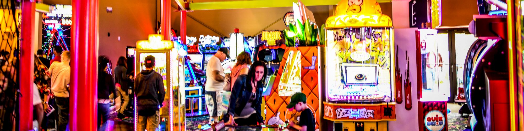 This image shows a vibrant indoor amusement center with various arcade games and a rope course overhead, with people enjoying the activities.