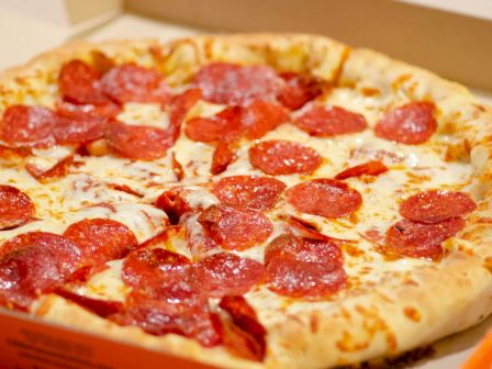 A freshly-baked pepperoni pizza in an open box, featuring a golden-brown crust and melted cheese topped with generous pepperoni slices.