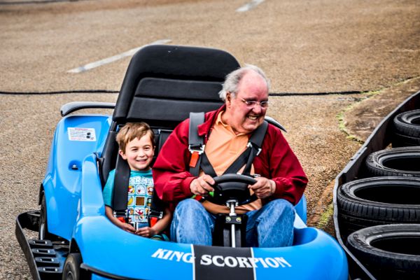 A smiling child and older man in a red jacket drive a blue 