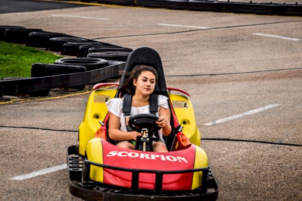 A person is driving a yellow and red go-kart on a racetrack, marked with 