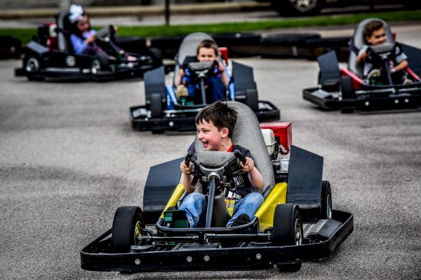 Children are enjoying riding go-karts on a track. They appear to be having fun and are focused on driving their vehicles.