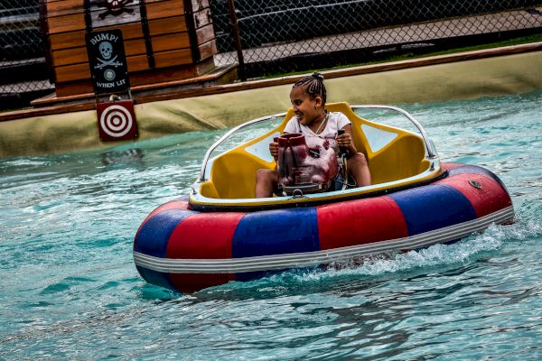 A person is riding a bumper boat in a pool, near a sign with a target and a 