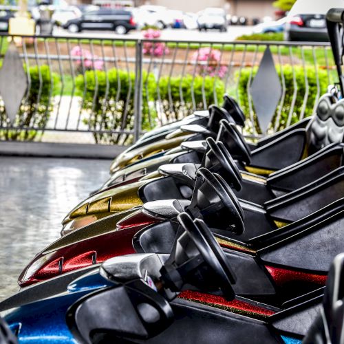 Bumper cars lined up in an amusement park ready for riders, with a fence and greenery visible in the background.