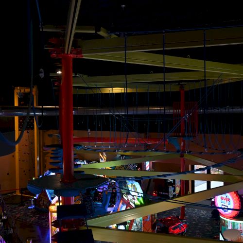 The image shows an indoor amusement area with an elevated ropes course and various arcade games and attractions underneath.