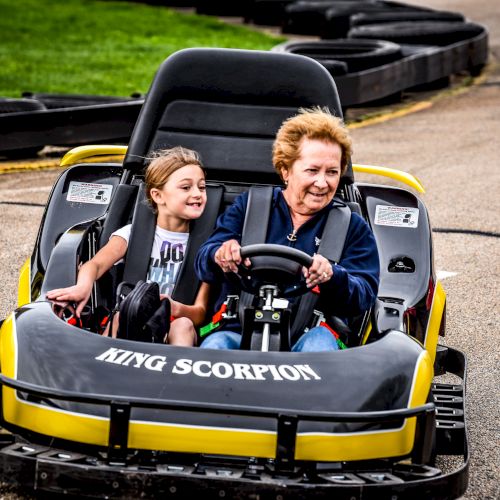 Two people, likely a woman and a child, are enjoying a ride in a yellow go-kart labeled 