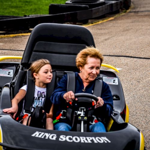 A child and an elderly person are riding a go-kart labeled 