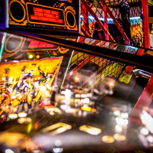 It is an image of a close-up view of a pinball machine in an arcade, reflecting vibrant lights and art designs.