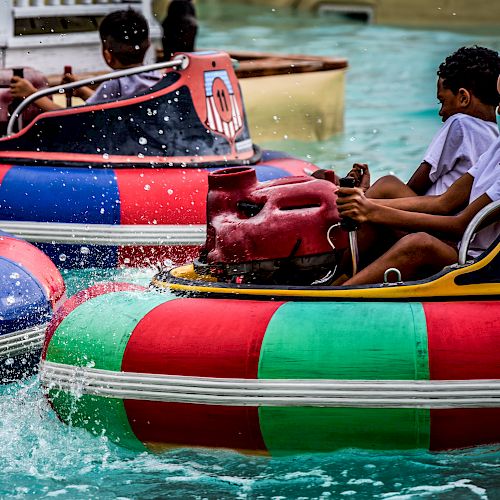 People are riding and bumping into each other with colorful bumper boats in a water ride, splashing water around.